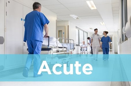 Acute Care Nurses: Image of hospital nurse pushing bed in hospital hallway past other hospital staff